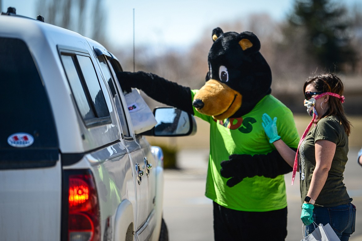 Cubbie the Bear and Lindsay Hecock, Kids Pastor at Canvas Church in Kalispell, hand out bags of Easter eggs and goodies to families in the parking lot of the church on Thursday. Canvas Church gave out over 1,000 bags containing around 22,000 eggs for the Easter holiday. (Casey Kreider/Daily Inter Lake)