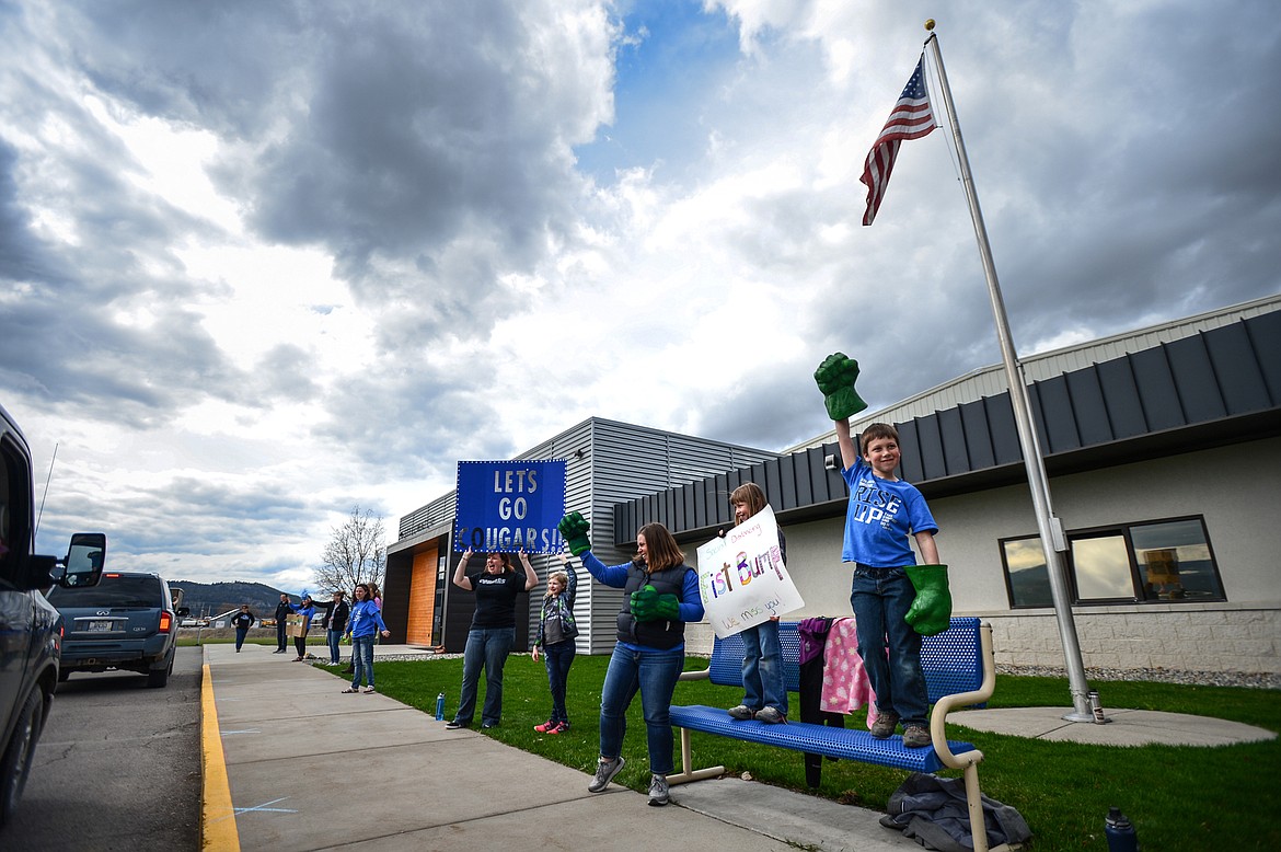 Stillwater Christian School bookkeeper Amy Orem and her daughter and son, Maddie and Henry, hold a sign and give fist bumps with Incredible Hulk hands during a parade for K-5 students and teachers outside the school on Friday, April 24. (Casey Kreider/Daily Inter Lake)