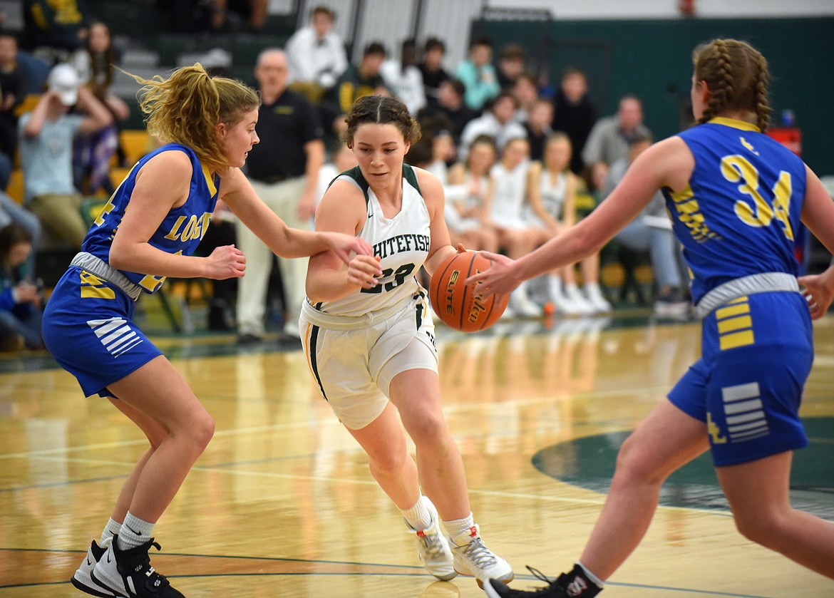 Bulldog Gracie Smyley drives between two Libby defenders Friday night at the Whitefish High School gym. (Heidi Desch/Whitefish Pilot)