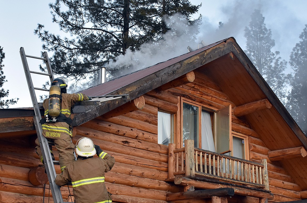 Neil Benson and Steve Lauer of the Libby Volunteer Fire Department battle a fire smoldering beneath the ridge cap of a home near Farm To Market Road on Feb. 21. (Duncan Adams/The Western News)