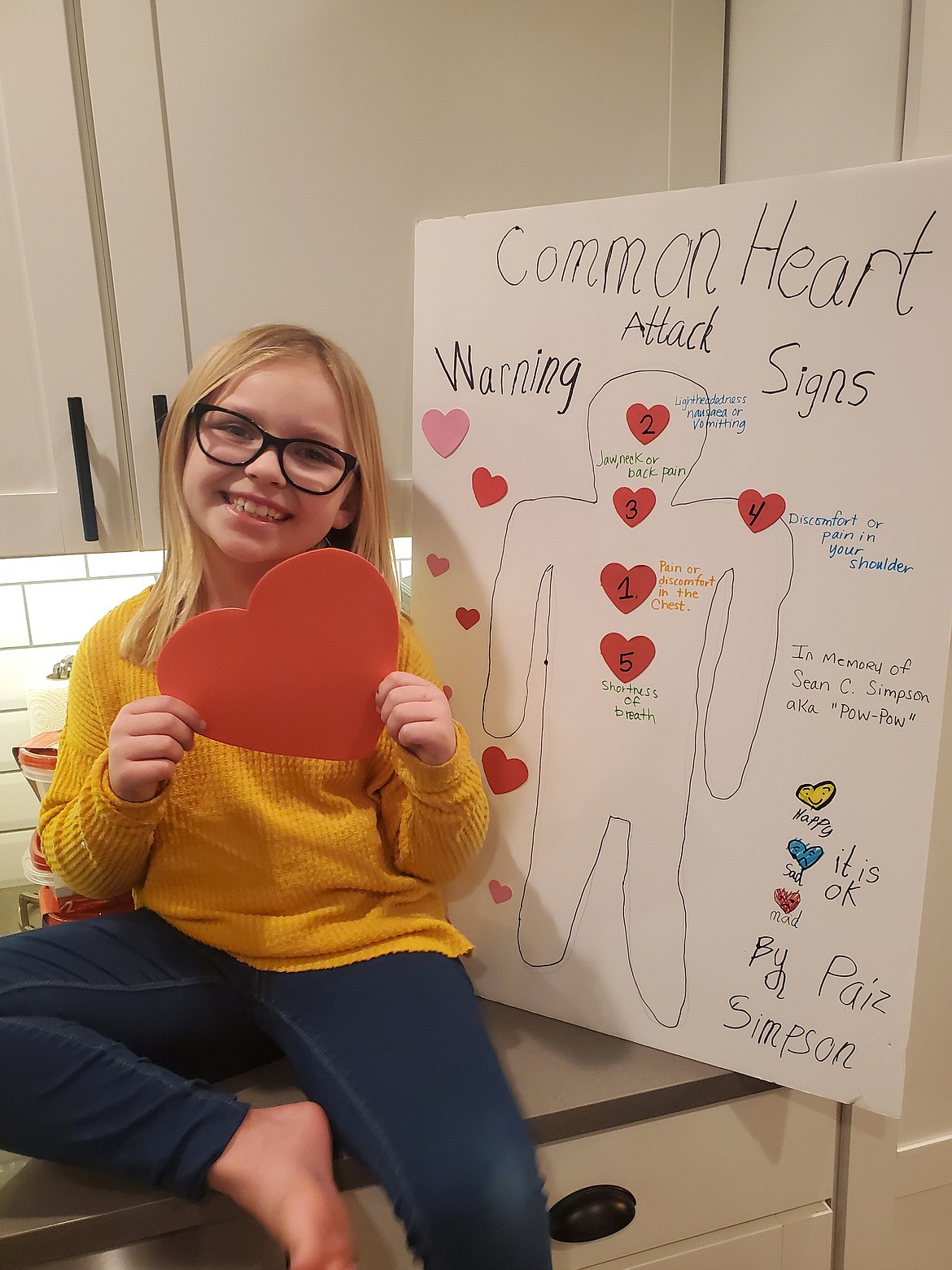 Paizley Simpson, 7, of Moses Lake, sits in front of the poster she made early in February to illustrate the common warning signs of heart attacks.