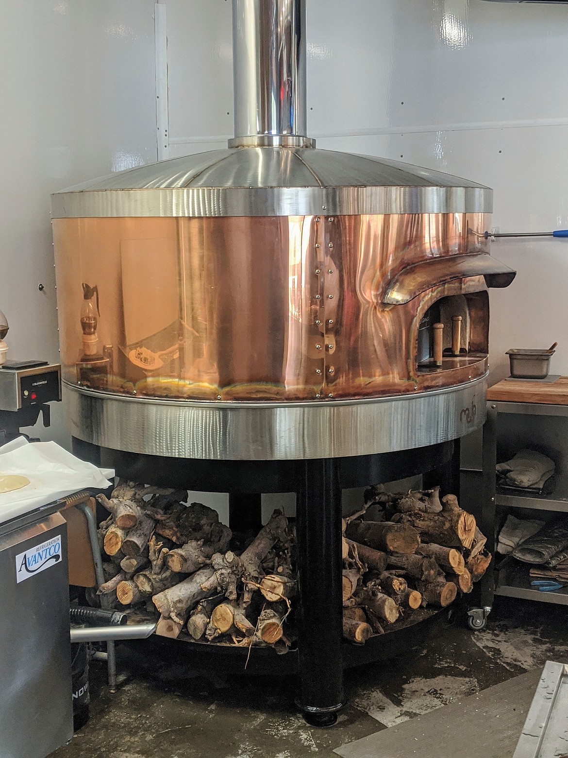 From the bar, one can see the exposed kitchen and wood fire pizza oven that truly is a work of art. Borrowing the look of an old fashioned copper still, this unique piece of kitchen machinery cooks pizzas around 750 degrees — roughly 250 to 150 degrees hotter than normal pizza ovens.