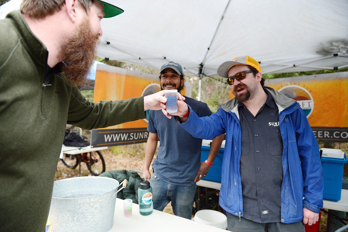 Paul Neff, left, takes an Over Under Belgian Dubbel from Ryan Weller, right, and Alex Stevens, center, from SunRift Beer Company at the Bigfork Brewfest at the Harry Horn Day Use Area of Wayfarers State Park on Saturday, March 7. (Casey Kreider/Daily Inter Lake)