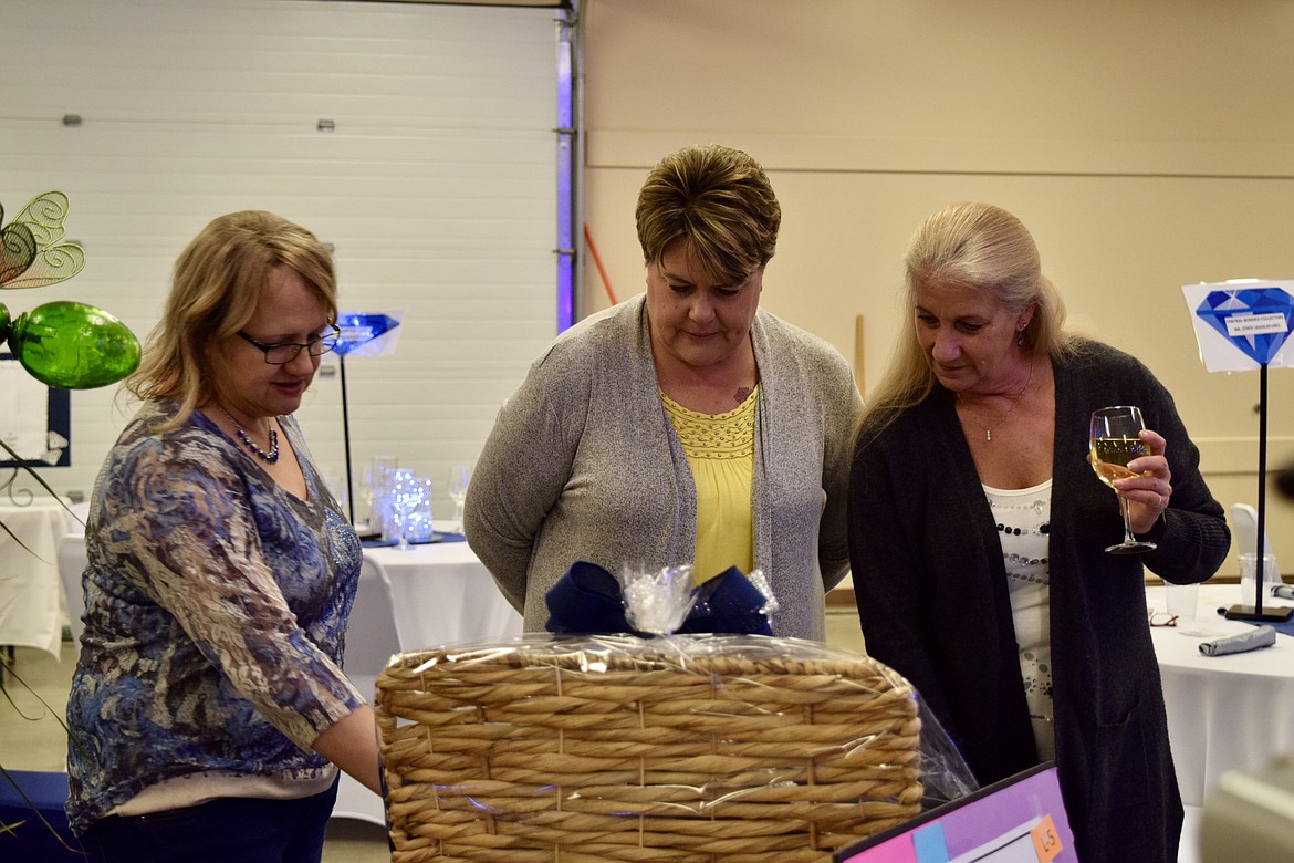 Charles H. Featherstone/Columbia Basin Herald 
 Melanie Strevy, Christy Harless and Cecilia Kimmel examine the Denim & Diamonds basket and, below it, the tickets to see country singer Chris Stapleton at the Gorge in late June. The items were up for bid in the live auction at the Moses Lake Chamber of Commerce's Denim and Diamonds fundraiser at the Grant County Fairgrounds on Friday.