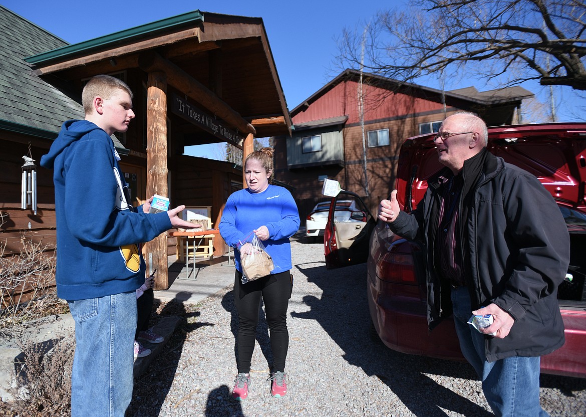 Roger Zanlandingham, right, flips a carton of milk to Jeremy Patton, left, as Dani Potts puts a pair of grab-and-go meals into a Ziplock bag for Patton outside Bigfork ACES on Wednesday, March 18.