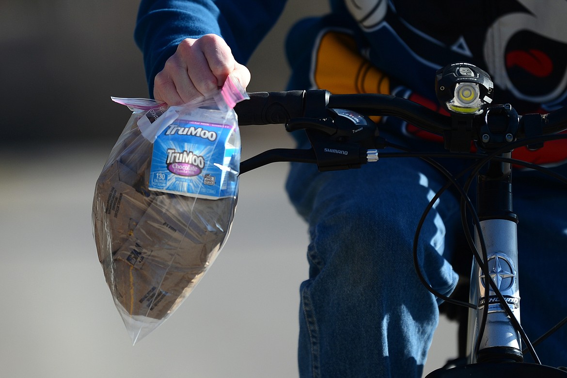 A youngster rides his bike holding a pair of grab and go meals outside Bigfork ACES on Wednesday, March 18. (Casey Kreider/Daily Inter Lake)