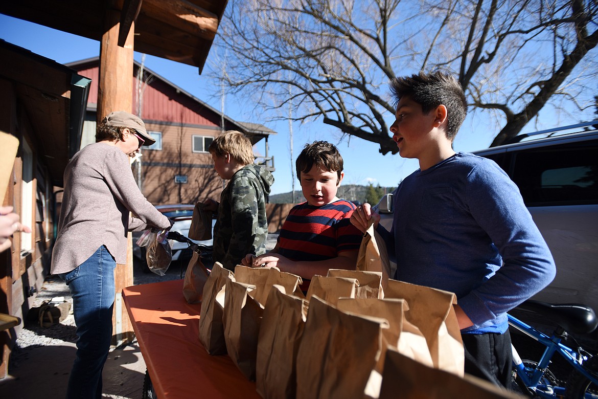Youngsters pull up on their bikes and get grab and go meals from Cathy Hay, site coordinator with Bigfork ACES on Wednesday, March 18. (Casey Kreider/Daily Inter Lake)