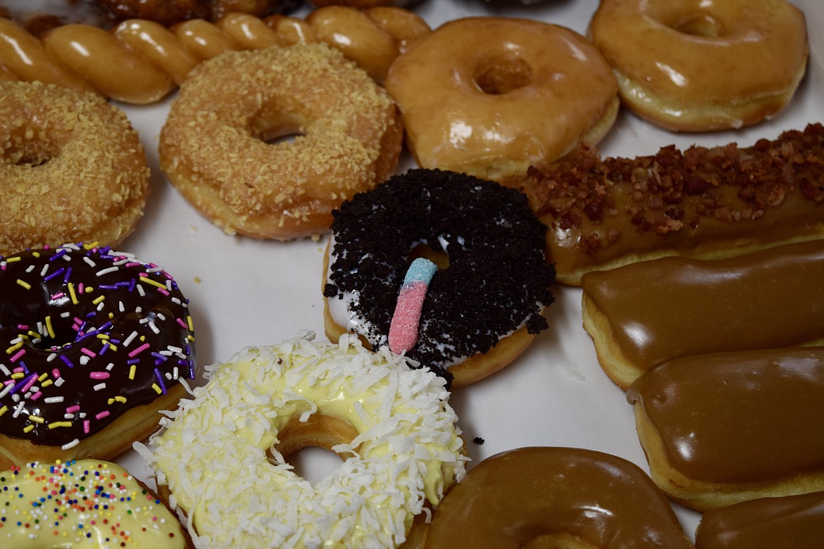 A collection of donuts. The donut with the gummy worm is covered with crushed Oreo cookies made to look like dirt.