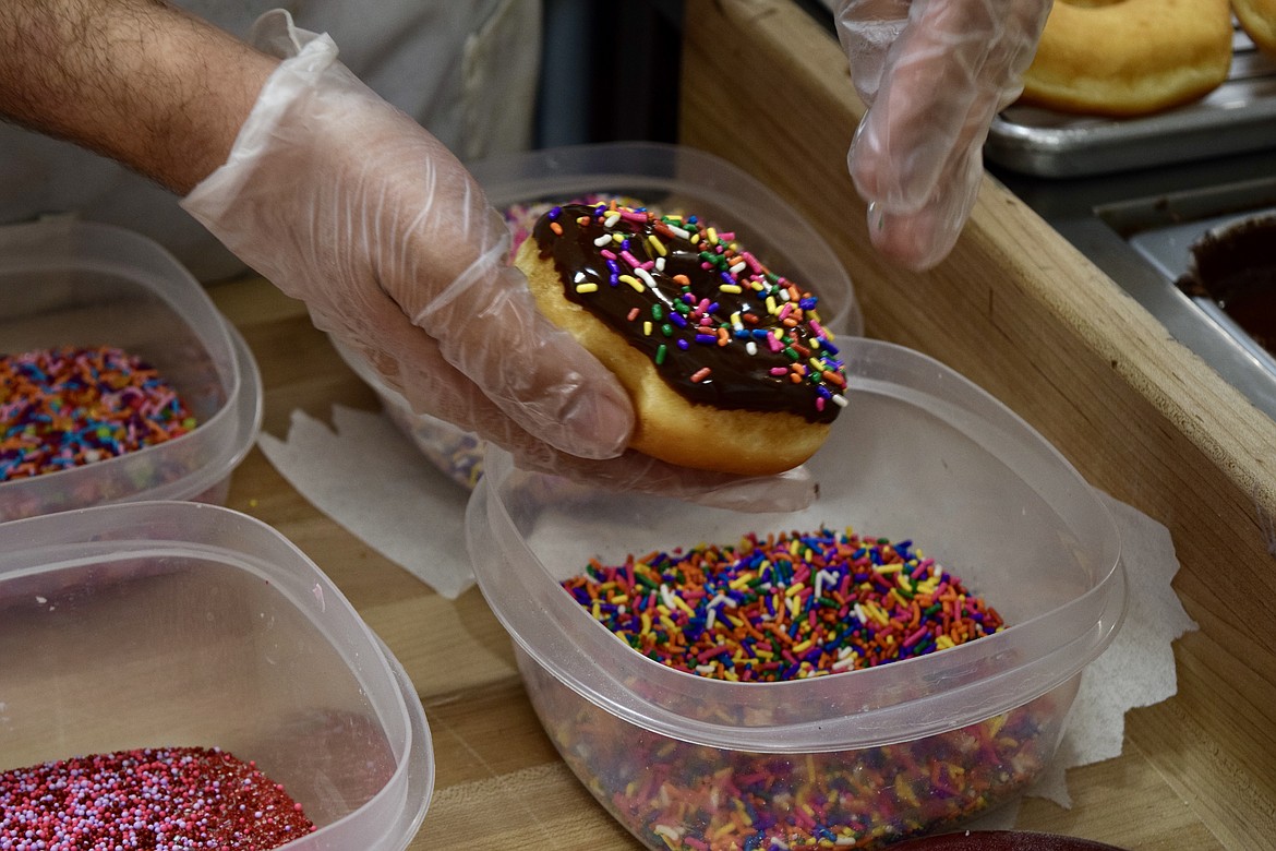 Troy Boorman adds sprinkles to a chocolate glazed donut.