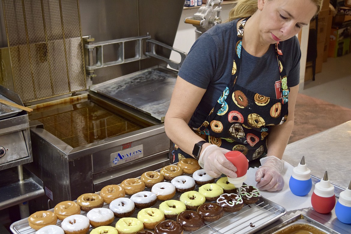 Lisa Boorman decorates some chocolate covered donuts with vanilla icing.