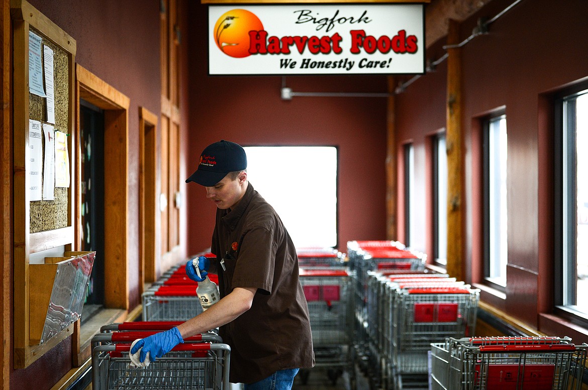 Colton Franklin sanitizes shopping carts inside the entrance to Bigfork Harvest Foods on Friday, April 3. (Casey Kreider/Daily Inter Lake)