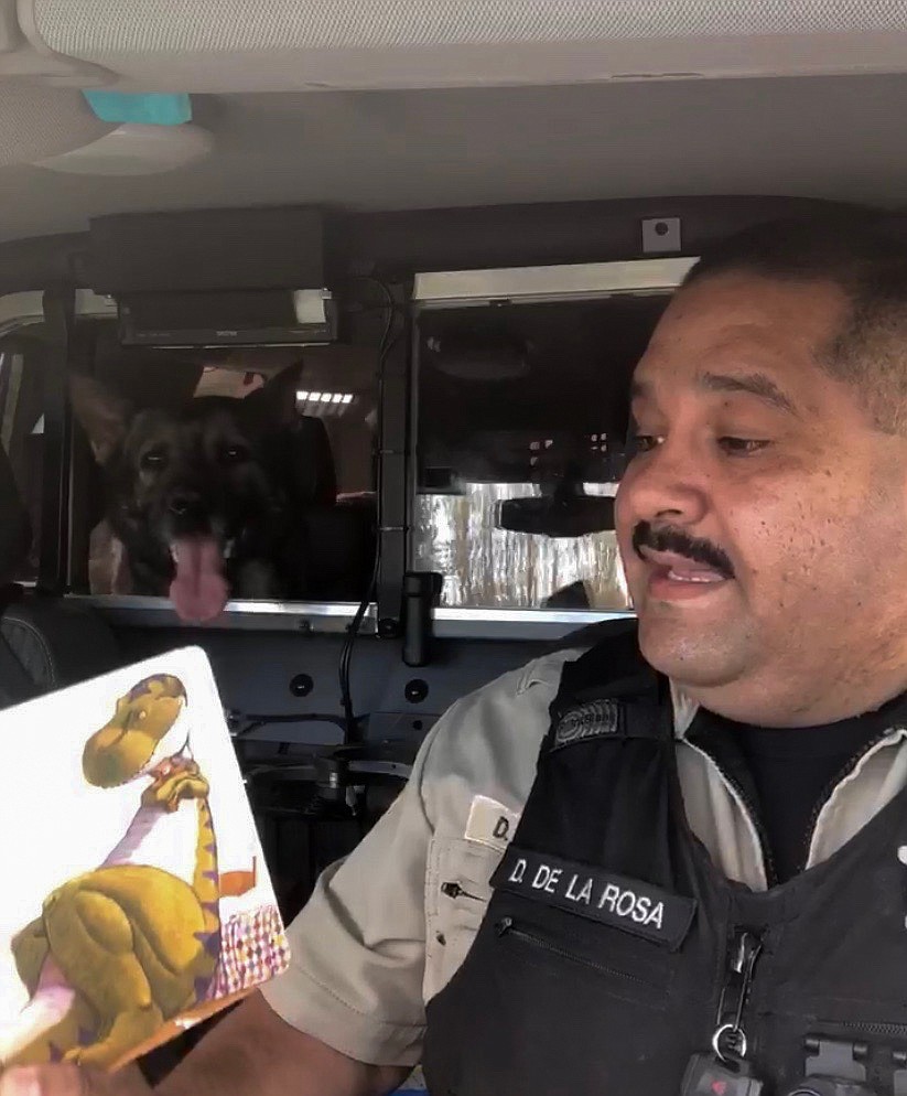 Deputy Dave De La Rosa reads to children at home in Spanish while K-9 Hawk waits patiently in the background.