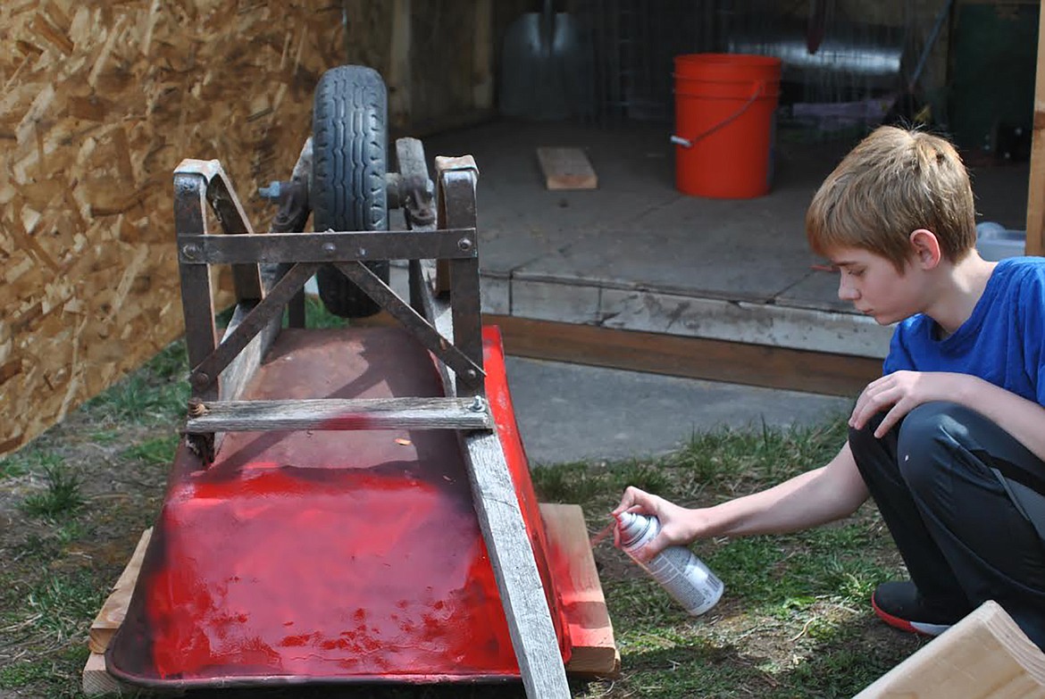 Hunter Farris spray paints a wheelbarrow red for the St. Regis School Community Gardens future strawberry planter. (Amy Quinlivan/Mineral Independent)