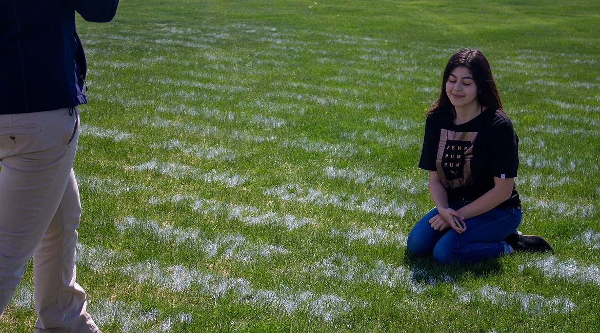 Moses Lake senior Dominique Flores-Bird kneels beside her name on the Field of Chiefs while her mother, Kitty Bird, takes a photograph on Monday.