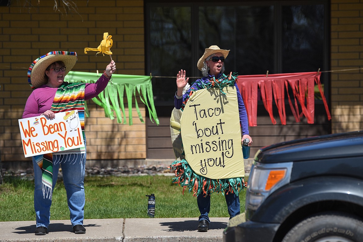 Second-grade teacher Sherry Bradstreet, left, and third-grade teacher Kate Butts wave and hold signs for students during a Cinco de Mayo Parade outside Swan River School in Bigfork on Tuesday. (Casey Kreider/Daily Inter Lake)