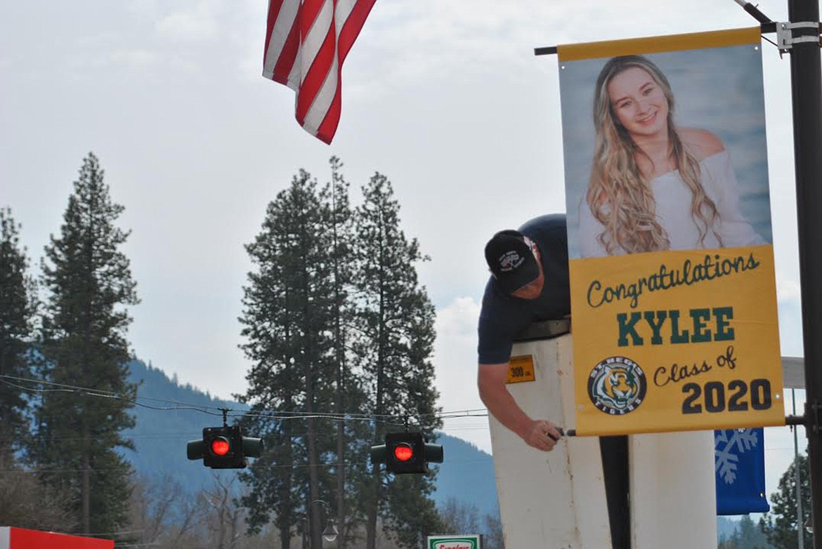 Kirk Willhite trades out the seasonal lamp post signs in St. Regis with ones celebrating this year’s seniors. (Amy Quinlivan/Mineral Independent)