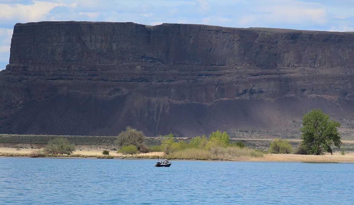 Clouds cast looming shadows on the side of Steamboat Rock in the distance as a lone angler sits in his boat on the waters of the Devil’s Punch Bowl on Monday, May 4.