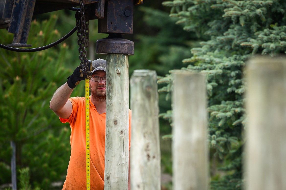 Jacob Christman, with Mild Fence Company, measures the height of a post as its driven into the soil during an installation near Creston on Wednesday, May 6.