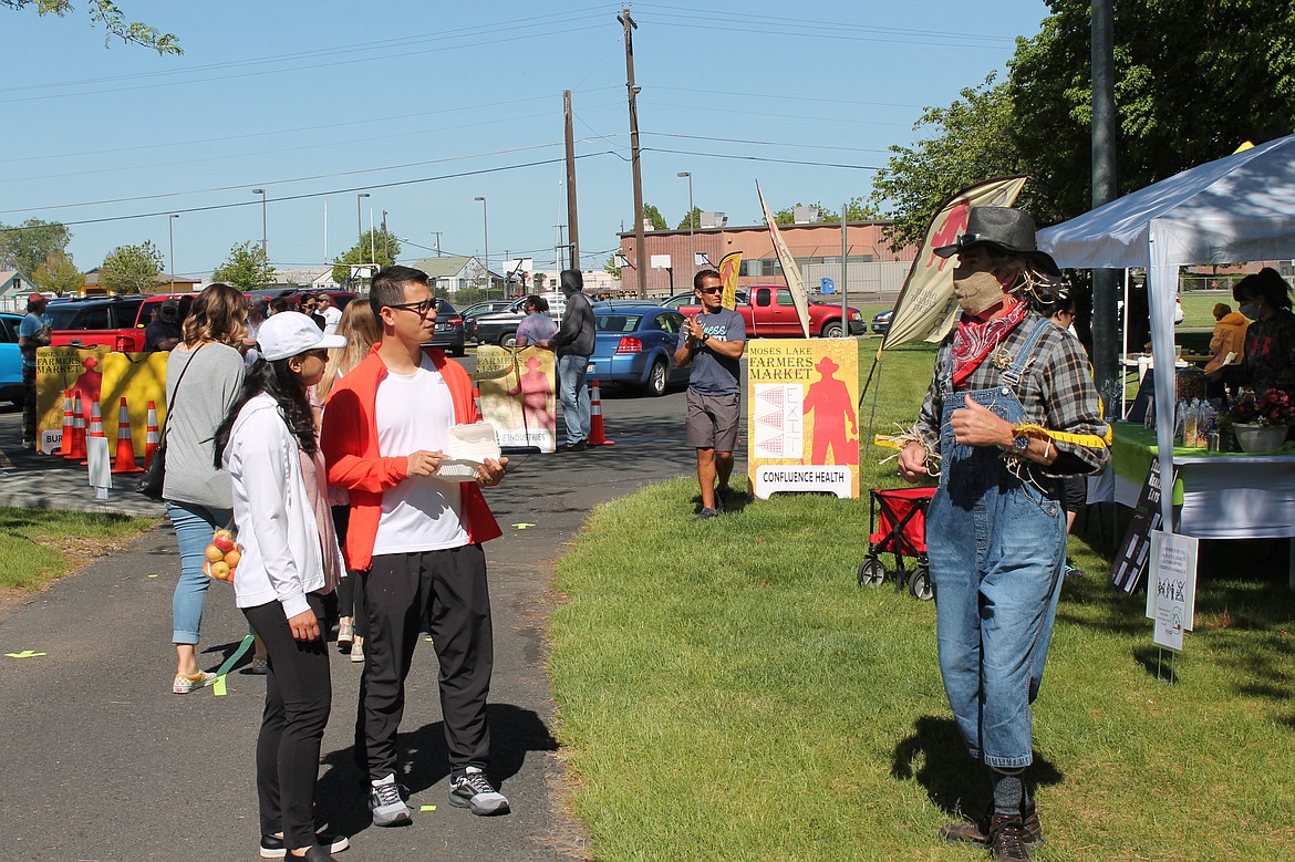 Martin Bosse, as the Scarecrowd, discusses social distancing and safety with Linh Nguyen, left, and Tung Nguyen at the Moses Lake Farmers Market Saturday.