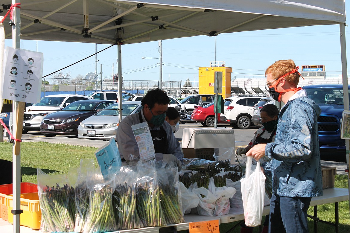 Joel Martin/Columbia Basin Herald 
 Santos Guadarrama of Royal Produce, left, serves a customer at the Moses Lake Farmers Market Saturday.