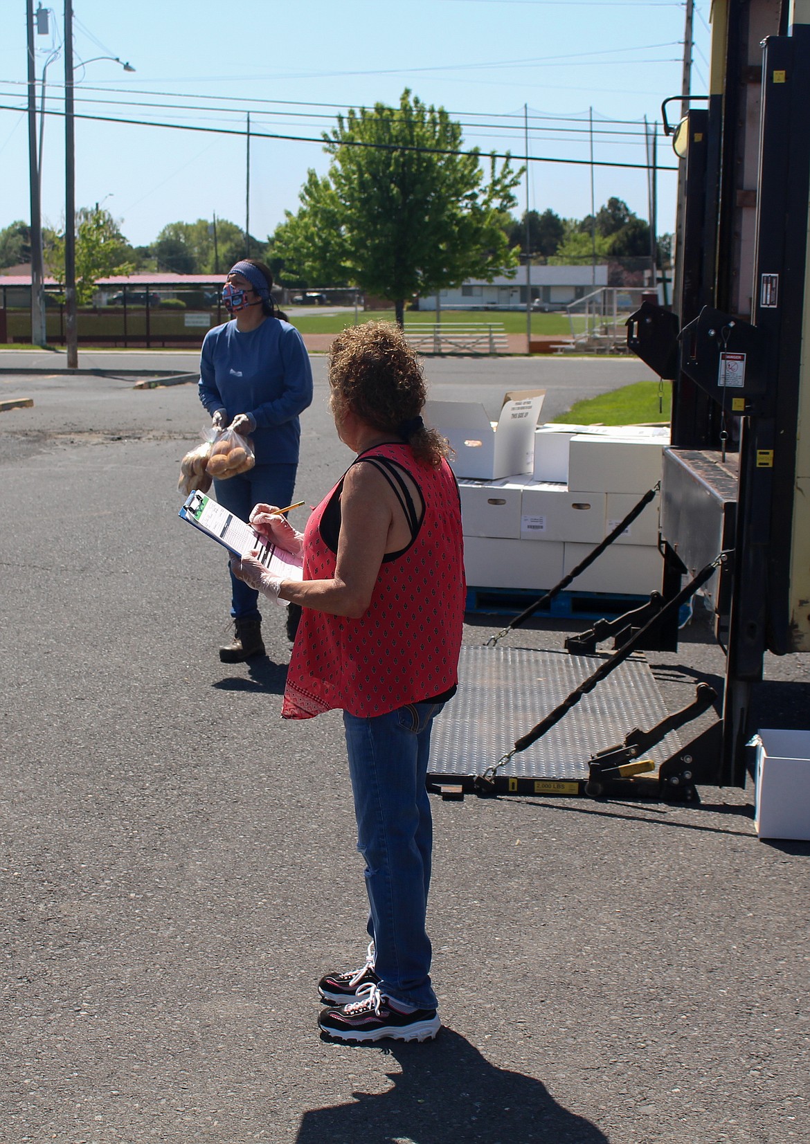 Casey McCarthy/The Sun Tribune 
 Jezabel Pinales, left, waits for the next car to pull up as Marina Barrera, looks over her checklist at the meal distribution stop at Othello High School last Thursday, May 7.