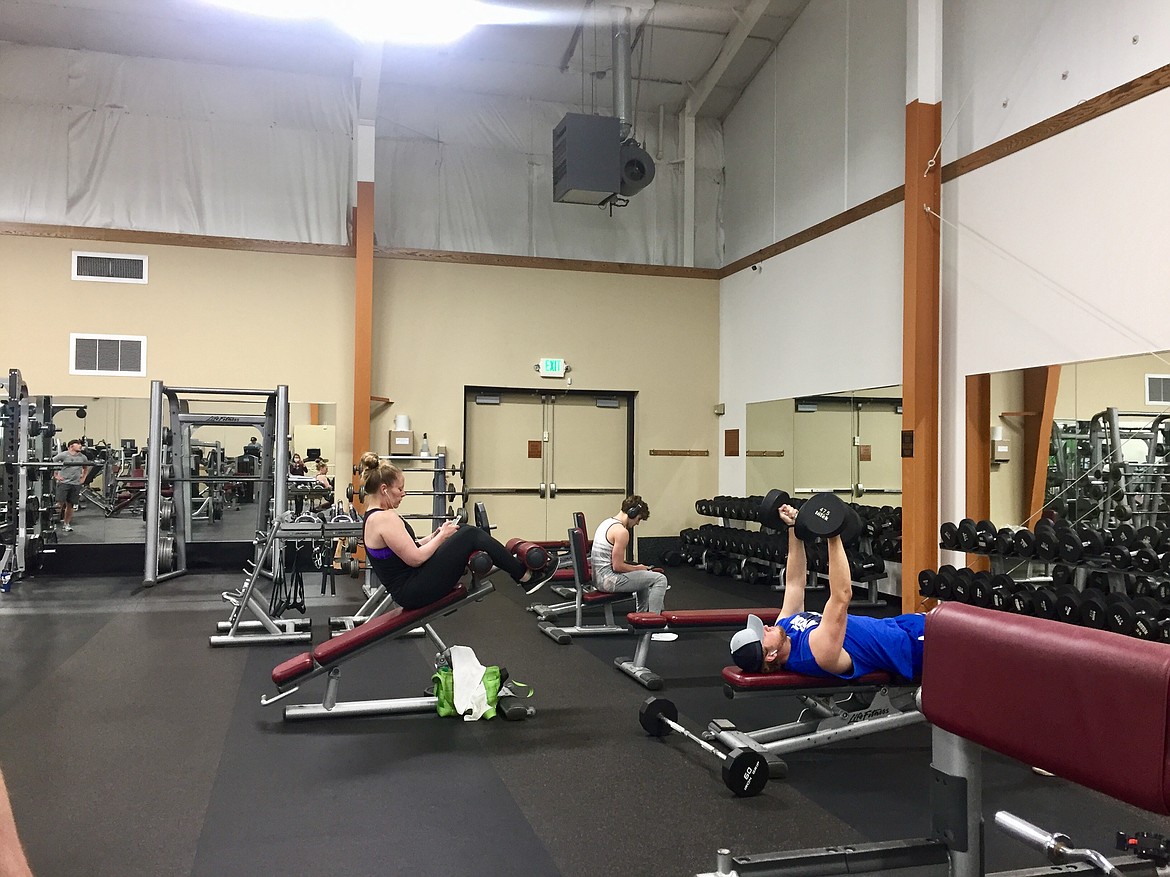 Members at Coeur d'Alene Peak lift weights and check their phones while maintaining social distancing requirements. The gym has taken precautionary measures to ensure safety as they reopening Saturday. (JENNIFER/PASSARO Press)