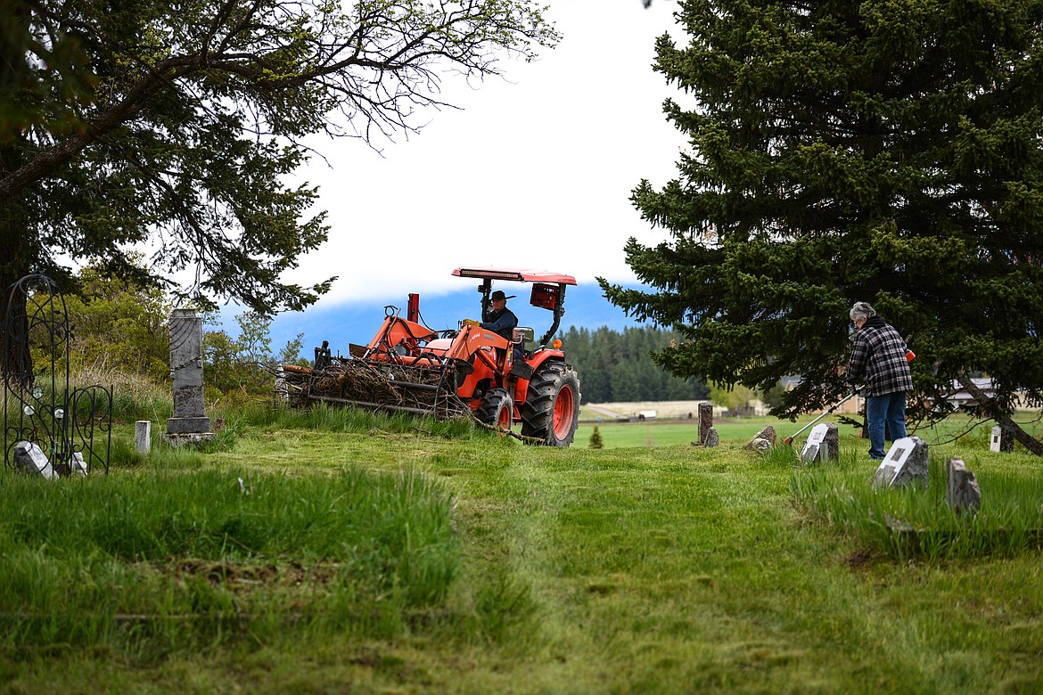 Tim Darr scoops up piles up debris while Jessie Wade uses a weedwacker around gravestones during the annual cleanup at Lone Pine Cemetery in Bigfork on Friday, May 15. (Casey Kreider/Daily Inter Lake)