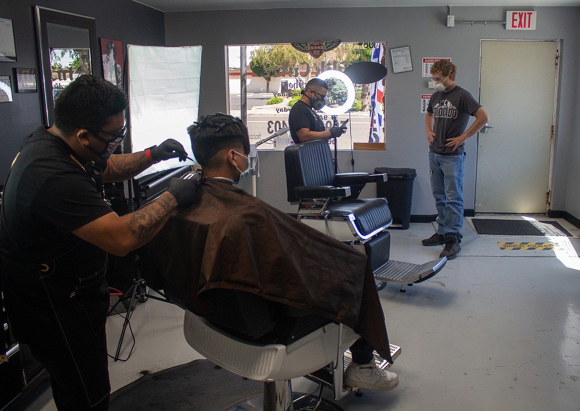 Barber Angel Tapia cuts the hair of client Gustavo Guzman in the foreground as Slik Cutzz owner Jesus Valencia, back left, sets up an appointment with a customer, Tony Lauthan.