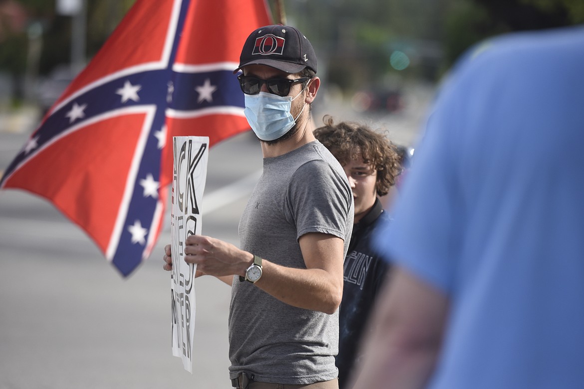 A Black Lives Matter protester holds a sign near a Confederate battle flag flapping in the wind along California Avenue. (Derrick Perkins/The Western News)