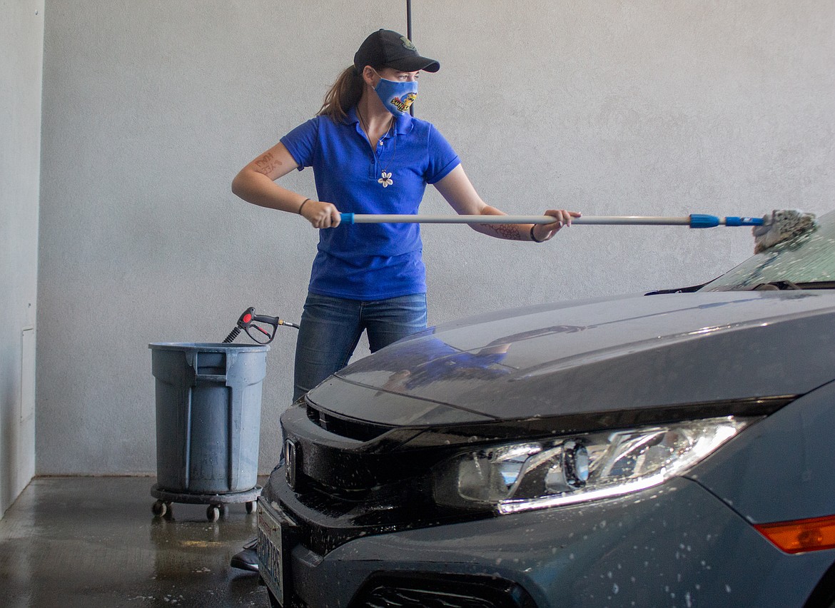 Jasmine Erdmann, an employee at Sun Splash Car Wash, cleans a windshield on Tuesday afternoon as the local car wash celebrates six months in business.