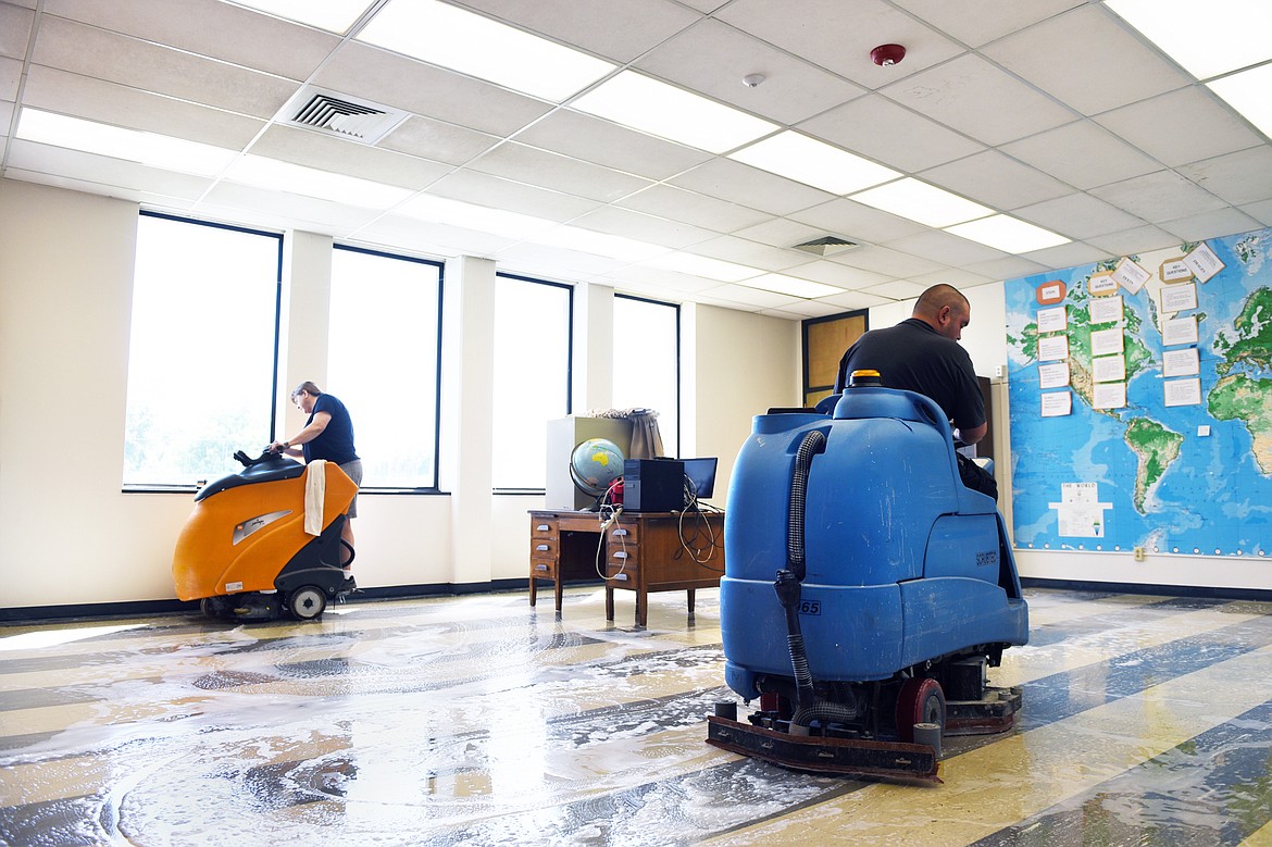 Custodians Dorene Conklin, left, and John Alton use industrial floor scrubbers before applying a fresh coat of wax to a classroom floor at Flathead High School on Wednesday, July 15. (Casey Kreider/Daily Inter Lake)