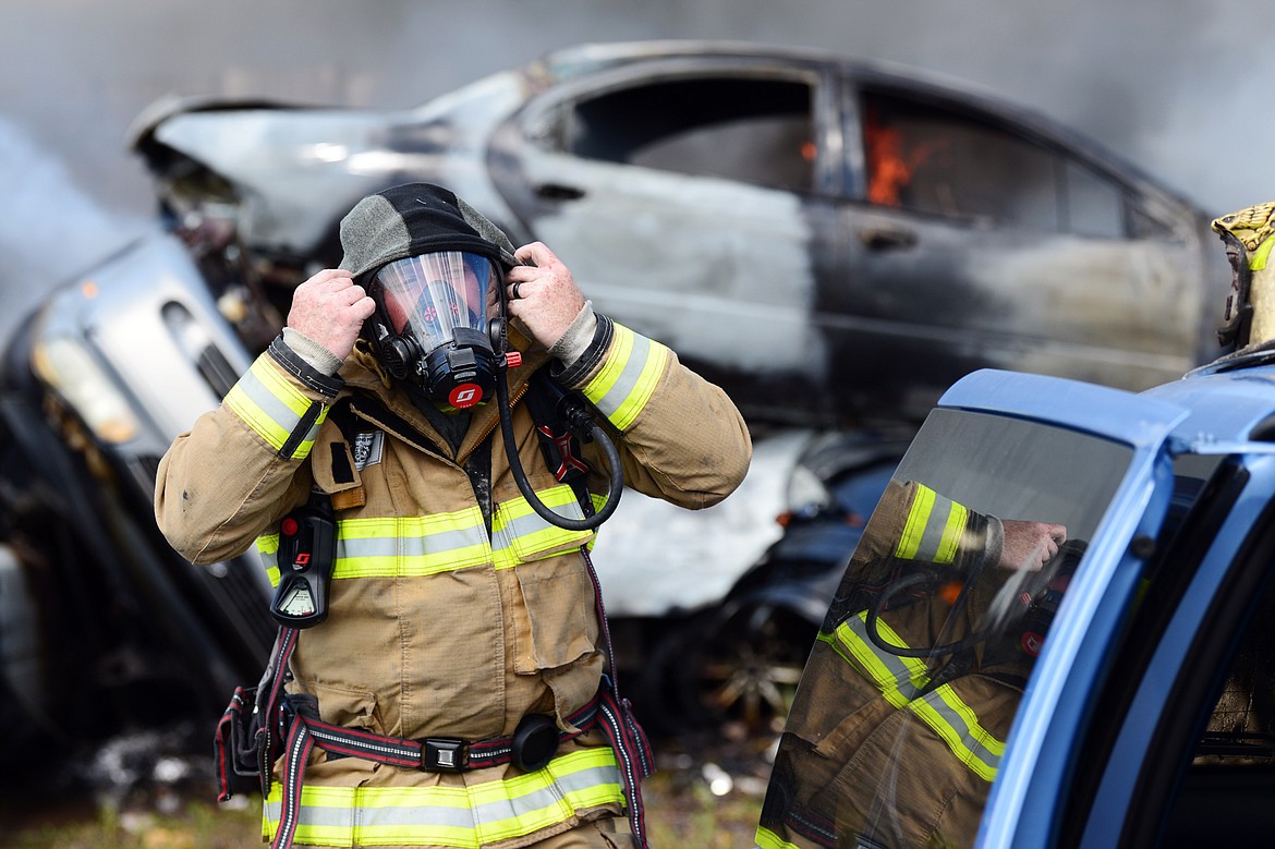 Evergreen Fire Rescue Fire Marshall Ben Covington puts on a mask at the scene of a fire in several vehicles in the junkyard at Tri City Auto & Wrecking along U.S. Highway 2 East near Glacier Park International Airport on Wednesday. Columbia Falls and West Valley fire departments also responded to the fire, as well as GPIA’s Aircraft Rescue and Firefighting vehicle. (Casey Kreider/Daily Inter Lake)