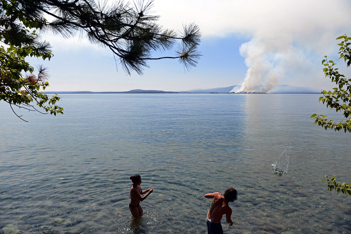 People skip stones from a roadside pullout on Flathead Lake along Highway 35 as a wildfire burns on Bird Island near Finley Point on Tuesday, Aug. 4. (Casey Kreider/Daily Inter Lake)