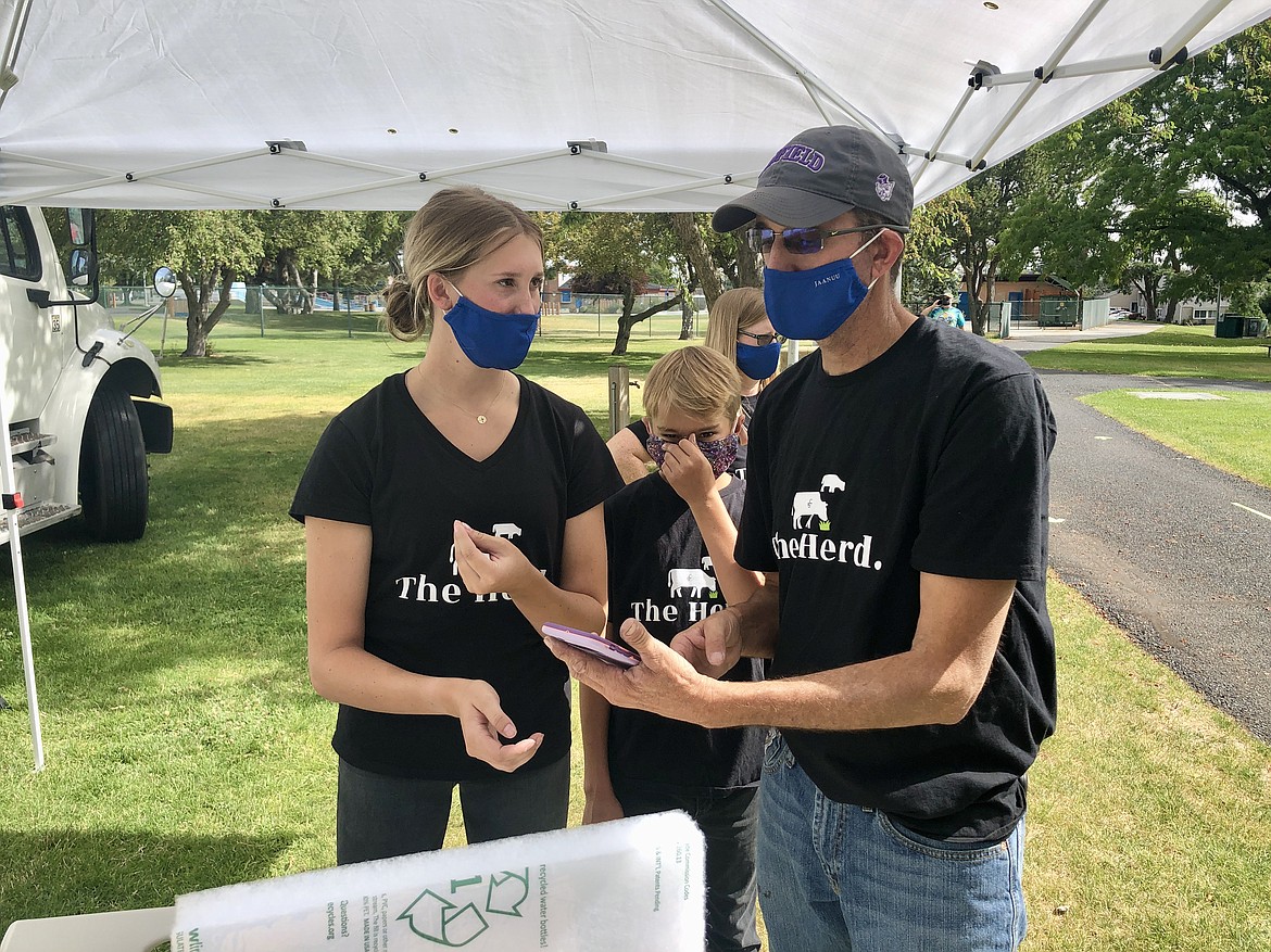 Charles H. Featherstone/Basin Business Journal 
 Peyton Curtis, 20, founder of the mail order beef business The Herd, shows her father Miles how to ring up an order on a cell phone at the Moses Lake Farmers Market on Saturday, Aug. 8.