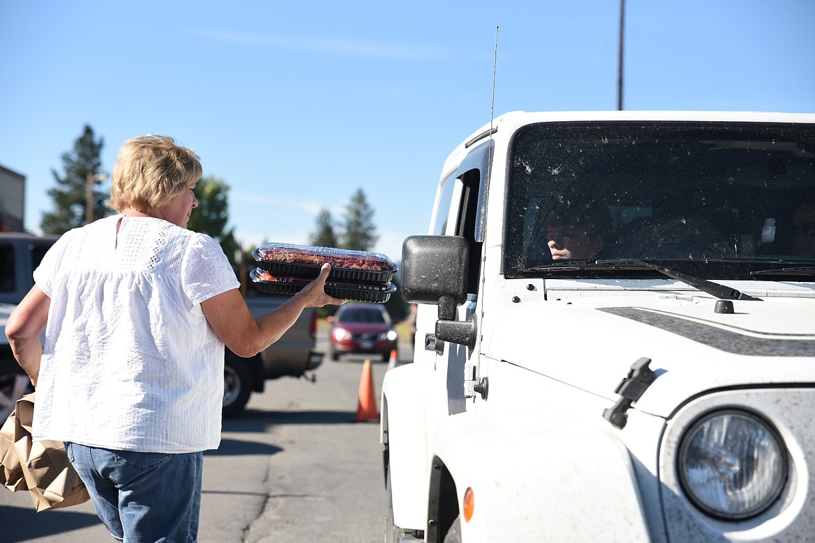 Linda Ramondelli hands a set of baby back ribs through the passenger window of a Jeep. The ribs were smoked by TJ Boswell for former servicemen and women to raise awareness about veteran suicide. (Will Langhorne/The Western News)