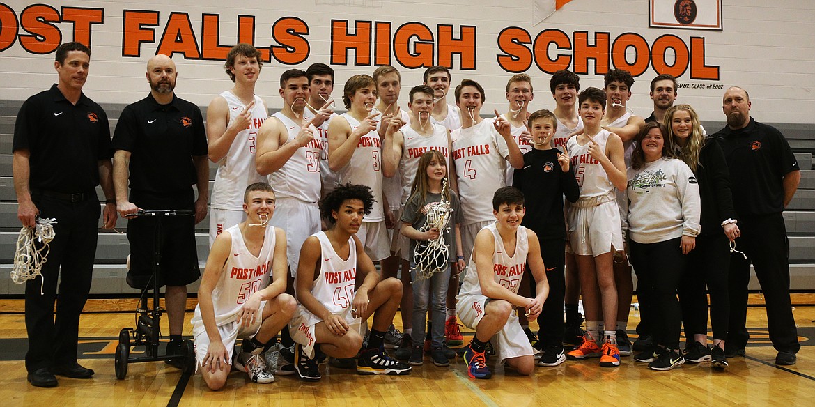 With head coach Mike McLean (second from left) perched on a knee scooter, the Post Falls basketball team poses with the 5A Region 1 championship trophy last week after defeating Lewiston.