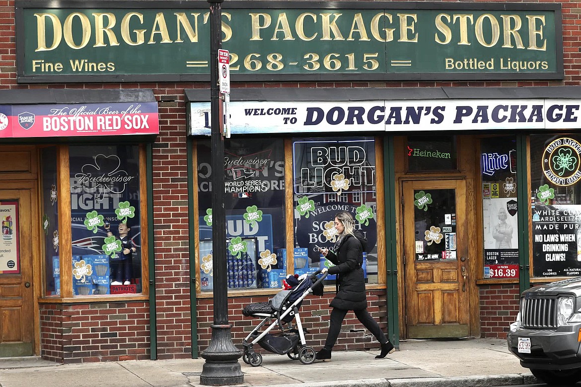 A woman pushes a stroller past a liquor store on a nearly empty sidewalk on Broadway on St. Patrick's Day in the South Boston neighborhood of Boston, Tuesday, March 17, 2020. For most people, the new coronavirus causes only mild or moderate symptoms. For some, it can cause more severe illness, especially in older adults and people with existing health problems. (AP Photo/Charles Krupa)