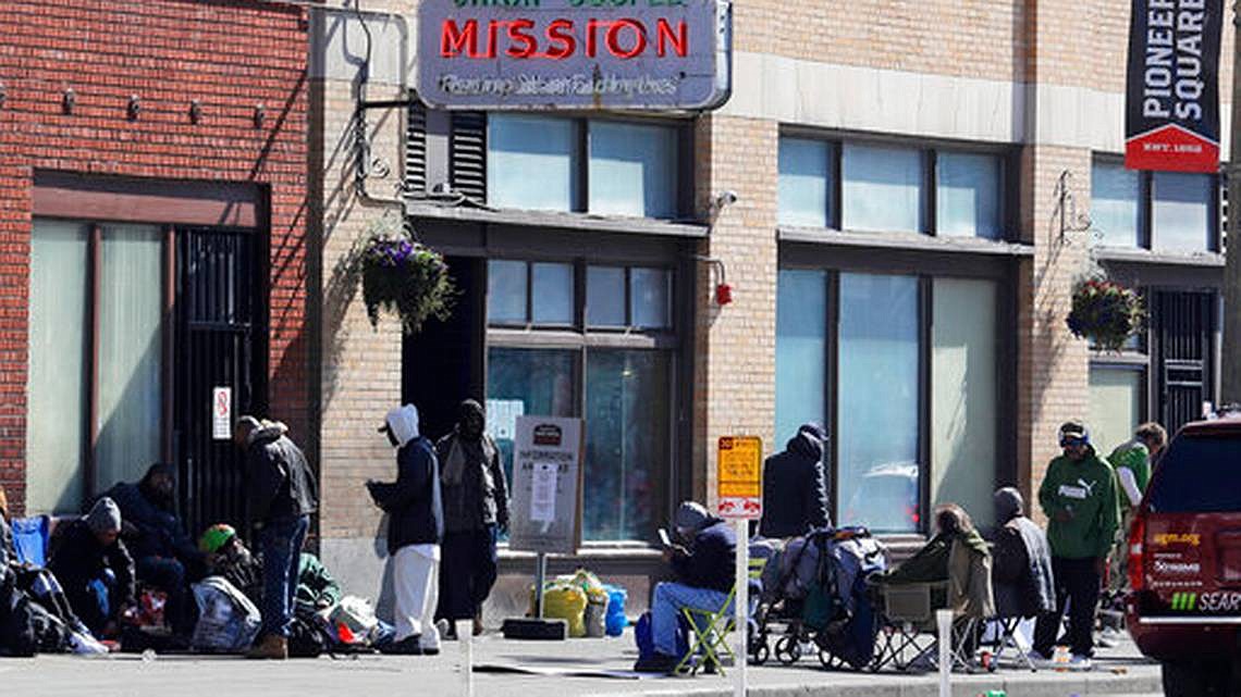 People gather on the sidewalk in front of the Union Gospel Mission in downtown Seattle, Friday, March 20, 2020. The Mission serves a large portion of Seattle's homeless population, and officials fear that controlling the spread of the new coronavirus in groups that lack access to basic hygiene and other supplies will be difficult. (AP Photo/Ted S. Warren)