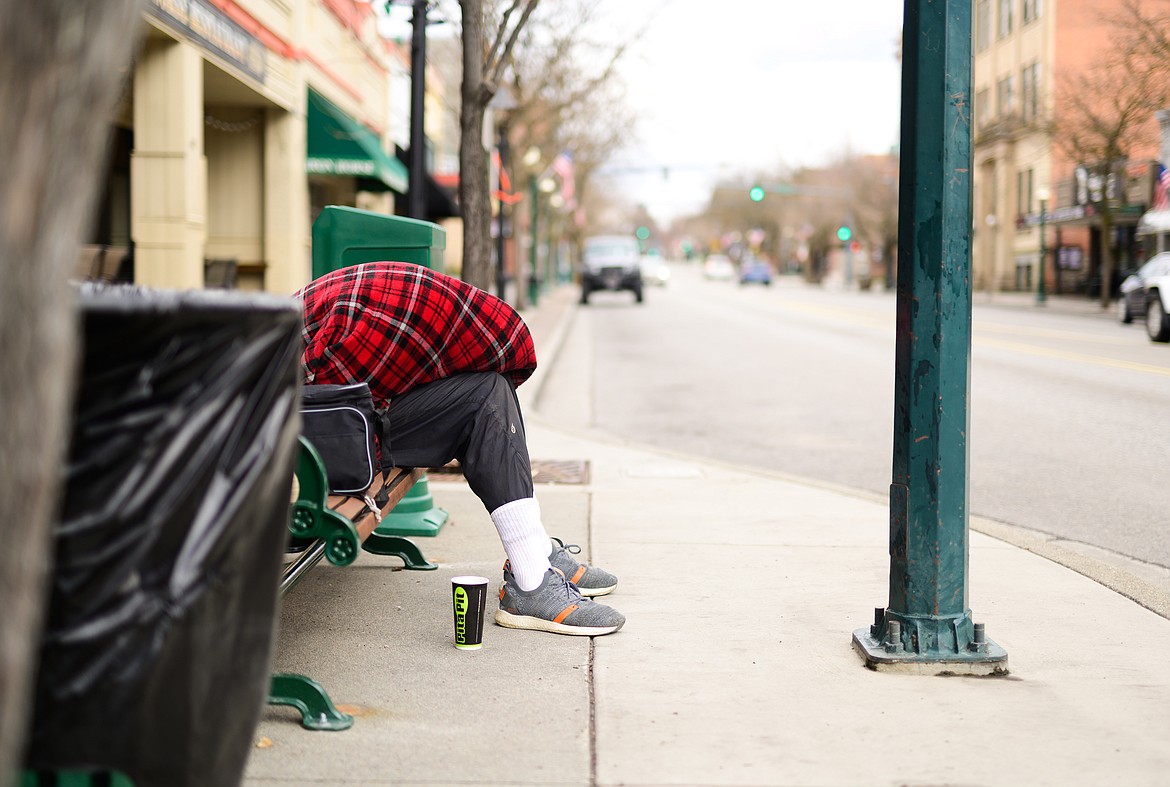 A man hunches under blankets on a bench on Sherman Avenue soon after stay-home orders are issued by Idaho Gov. Brad Little.
