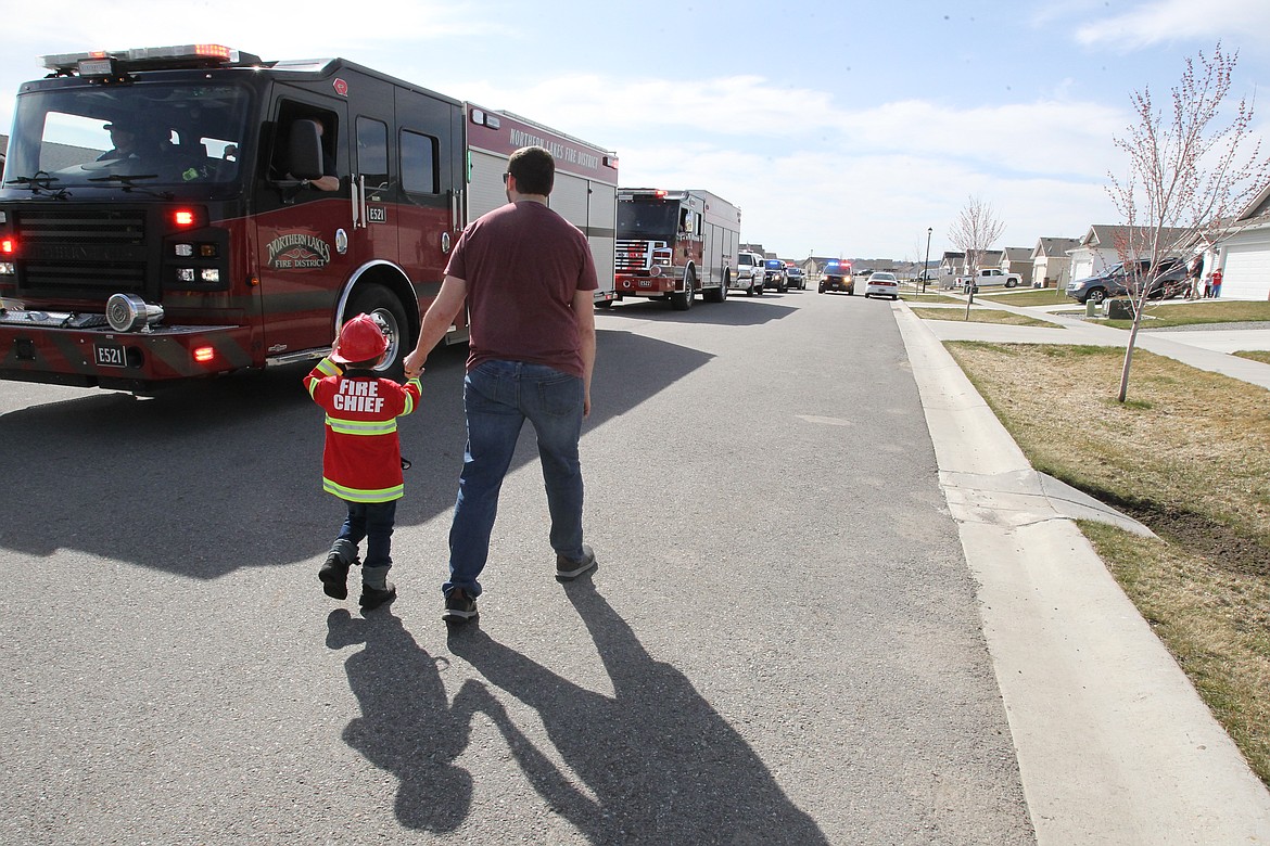 BILL BULEY/Press 
 Lukas Petroskie and dad Matt Petroskie walk along and check out the procession of fire trucks and police vehicles coming down their Rathdrum street Wednesday to celebrate the boy's fourth birthday.