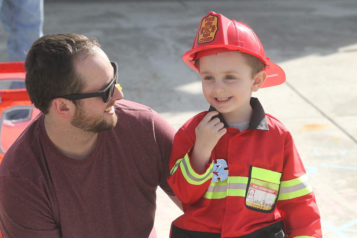 Lukas Petroskie, with dad Matt Petroskie, smiles at the procession of passing fire trucks and police cars outside his Rathdrum home Wednesday.