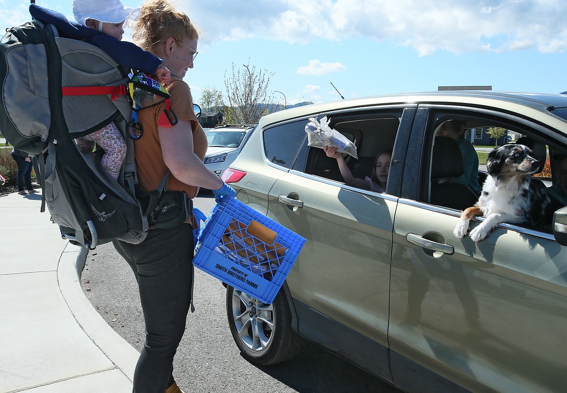 Greensferry Elementary School first grade teacher Anna Hixson, with infant daughter Margo in tow, accepts Lois Chesley’s work packet for April during a “reverse parade” and packet exchange at the school Monday. Mini-Australian shepherd Shellbee enjoyed riding shotgun.