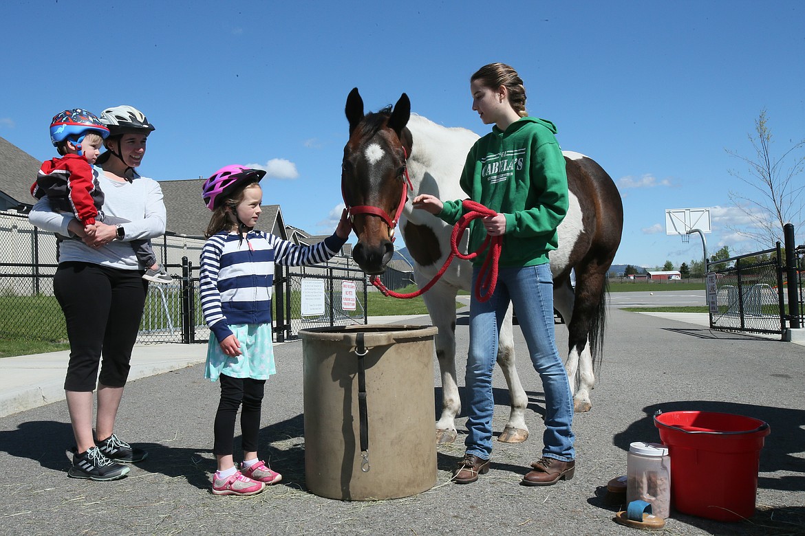 Greensferry Elementary volunteer Sterling Coy and Bird the horse make friends with first-grader Ellie Munson, who rode her bike to the school with mom Betsy and little bro Levi, 2, during a work packet exchange and “reverse parade” on Monday.