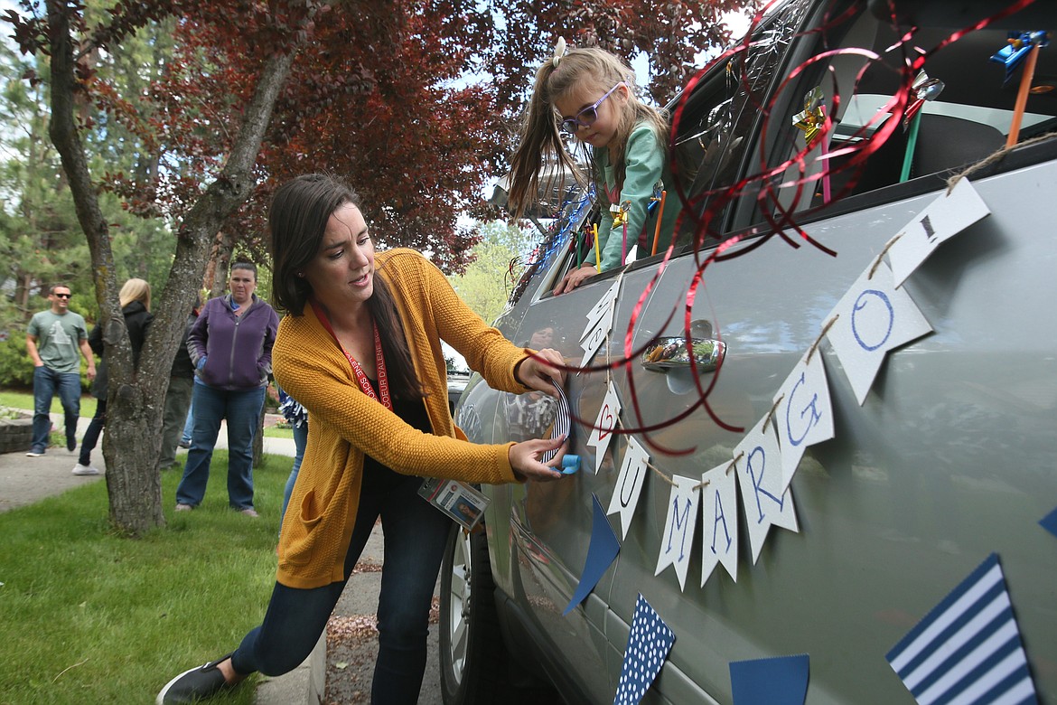 Lakes seventh grade English language arts teacher Jeni Nelson tapes a banner to her car Thursday as 4-year-old daughter Charlotte supervises during a surprise drive-by celebration for Margo Swanson, Coeur d'Alene School District's Teacher of the Year. (DEVIN WEEKS/Press)