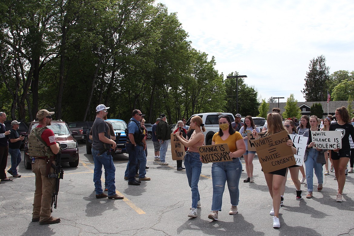 (File photo/KEITH KINNAIRD) 
 Protesters pass by armed adults at the Bonner County Courthouse. That private paramilitary activity during that peaceful Black Lives Matter protest earlier this month violated the Idaho Constitution and state law, according to the Institute for Constitutional Advocacy & Protection at Georgetown University in Washington, D.C.