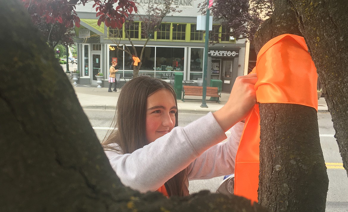 BILL BULEY/Press 
 Marissa Bershaw places a orange ribbon around a tree on Sherman Avenue Friday morning in recognition of National Gun Violence Awareness Day.