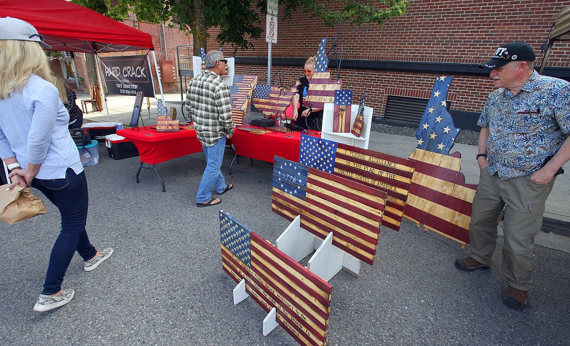 BILL BULEY/Press 
 Bob Shay, right, and others customers visit with Leah Loffer of Rustic Glory Flags at the Kootenai County Farmer's Market on Wednesday in Coeur d'Alene.