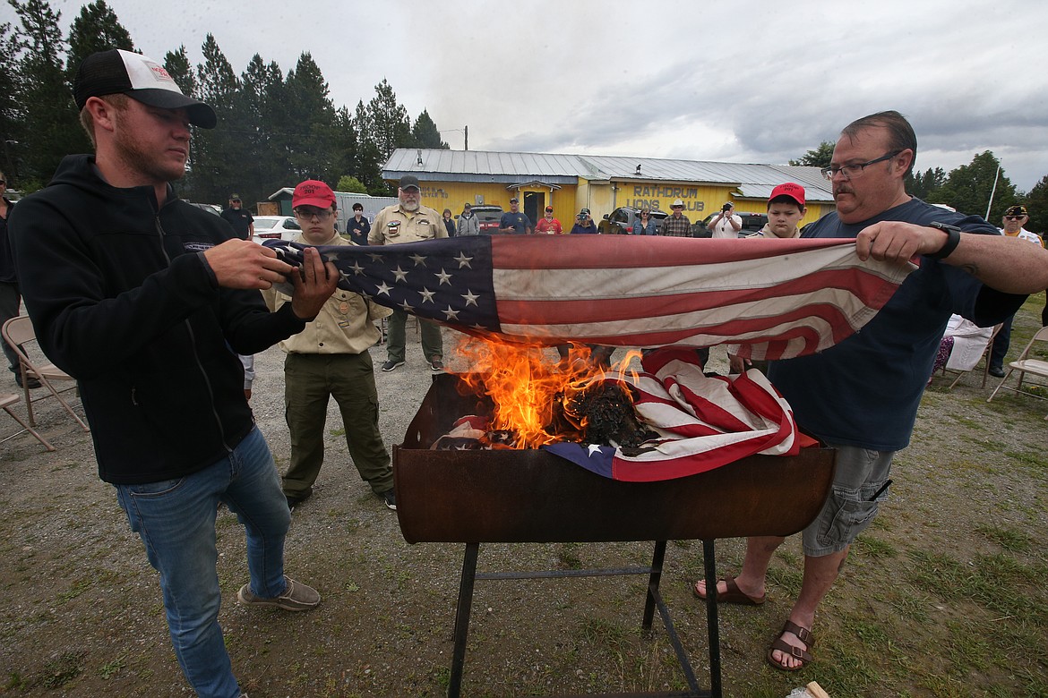 BILL BULEY/Press 
 Caretakers of the fire, Michael Montee, left, and Jeffrey Broadhead place another flag into the flames on Saturday at the Rathdrum Lions Club.