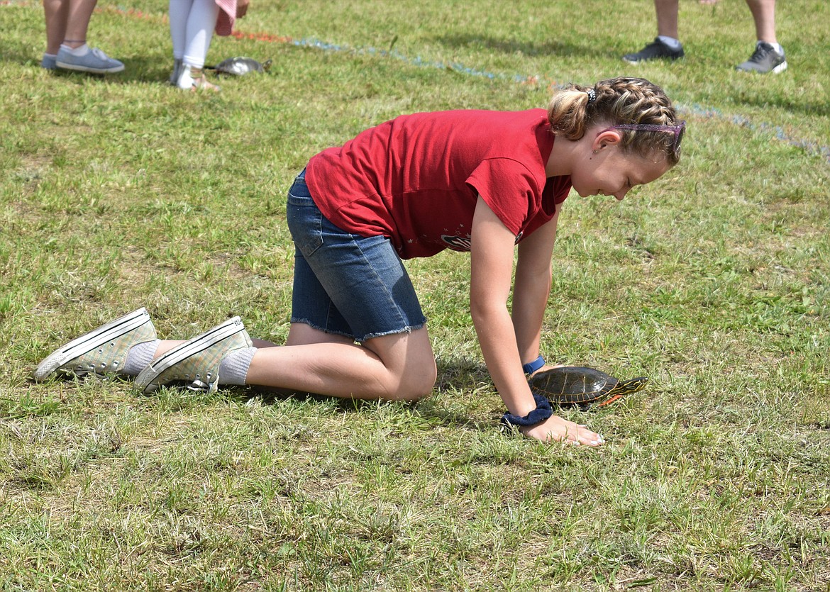 (Photo by DYLAN GREENE) 
 A young girl smiles as she crawls with her turtle toward the finish line.