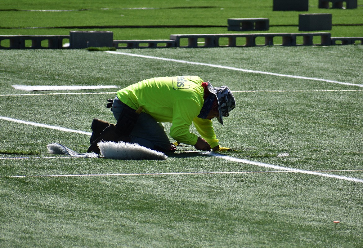 A worker sews in hash marks on the new artificial turf Wednesday.